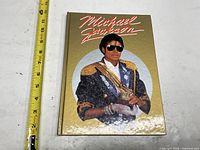 Front cover showing gold background, red script title and portrait of Michael Jackson with measuring tape for scale