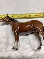 Full side view of brown glazed porcelain horse figurine with measuring tape showing length about 7 inches