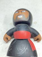 Front view of Mighty Muggs figure showing face, torso, red sash and wear