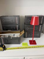 Six boxed lamps with one assembled red lamp showing design and size next to measuring tape