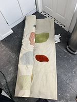 Rug partially unrolled showing off-white backing and coloured shapes