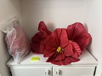 Three assembled large red paper flowers with yellow centres on shelf