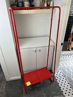 Full view of red metal clothing rack with shelf installed