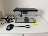 Front view of glass aquarium with hood, filter visible inside, net and power cord on surface