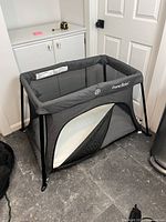 Front three-quarter view of assembled grey Pamo Babe travel crib with mattress inside