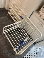 Disassembled white metal toddler bed frame with headboard, footboard and slatted base sections taped together