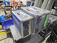 Three blue AVW-TELAV flight cases stacked on cart showing top and side hardware