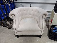Front angled view of beige tufted armchair with nailhead trim