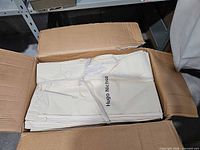Open box showing stack of folded beige garment bags tied with strap