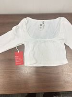 Front view of white ribbed long-sleeve crop top with tag