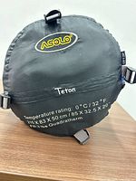 Front view of compression sack showing Asolo logo, model name, temperature rating, dimensions, and fill details
