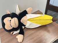 Full view of plush monkey with banana laid on table