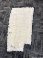 Full view of faux fur rug on floor showing irregular cut and staining