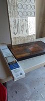 All three items on table: boxed Levolor blind, small framed wood-tone art, large vertical art panel behind