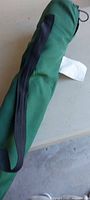 Green carry bag holding folded lawn chair, black strap visible