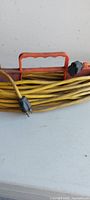 Side view of yellow extension cord coiled on orange plastic reel showing carry handle and plugs