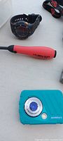 Close-up of wristwatch, UV Mini Flex light, and teal Polaroid camera