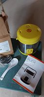 Rice cooker with lid, booklet, spoon and bubble-wrapped cord on table