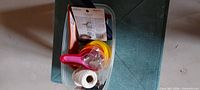 Grouped view of measuring cups, twine and packaged items in plastic container