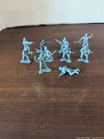 Seven of the ten grey plastic army men on wooden surface