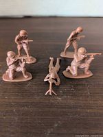 Five tan plastic army men on wooden surface