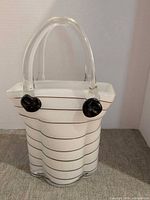 Full view of white glass purse-shaped decor with black stripes and clear handles