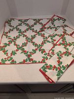 All five napkins spread and folded showing holly pattern and red border