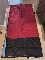 Sleeping bag laid flat showing red and black exterior with light blue lining
