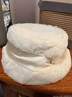 Exterior view of white faux fur hat showing satin band and rhinestone