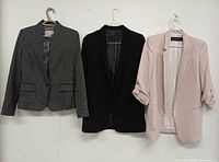 Three blazers displayed on hangers: charcoal pinstripe, black, blush pink