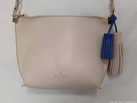 Front of beige Kate Spade crossbody bag showing logo and tassel