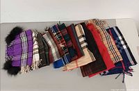 Row of approximately thirteen plaid scarves laid side by side showcasing variety