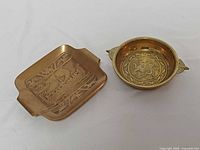Square brass tray with Viking longship next to round dragon dish