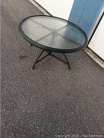 Round glass patio table shown at low height outdoors on pavement.