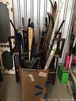 Multiple skis from various brands including Dynastar, Rossignol, Splitken, Laasanen, stored in a cardboard box showing tops and bindings of several skis.