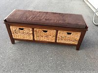 Front view of the brown storage bench with padded cushion and three woven baskets.