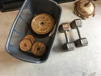 Photo showing plastic basket with various metal Weider barbell weights and two metal dumbbells with 25 lb markings on floor