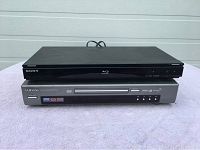 Top-down photo showing stacked Sony Blu-ray player and Samsung DVD player on a light purple cloth surface.