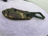 Photo showing the shovel partially inside the camouflage carrying case on a white cloth background.