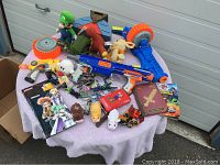 Full view of lot items on table showing Nerf guns, plush toys, books, and action figures.