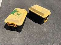 Two yellow-lidded black rolling storage bins with paint splatter and dirt marks seen from above on pavement.