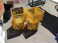 Four yellow plastic record crates stacked outdoors on pavement, some dirt visible on crates.