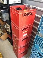 Stack of five red plastic Borden record crates with one crate holding a vinyl record sleeve.