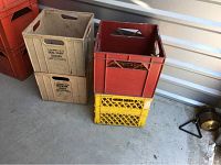Four plastic record crates stacked and arranged on the floor, showing the beige Ideal Dairy crates with labeling and the stacked red and yellow Dairyland crates.