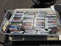 Top view of a plastic bin filled with numerous video game cases for various systems, arranged and stacked inside the bin showing a wide variety of titles mostly Xbox 360.