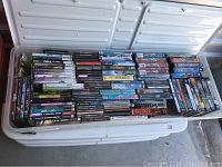 Large white plastic storage bin filled with video game cases stacked tightly showing various titles mainly Xbox 360 and PC games.