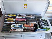 Plastic bin filled with assorted video game and movie cases showing titles and condition.
