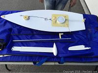 White radio controlled sailboat hull with rigging and listed components on blue mat