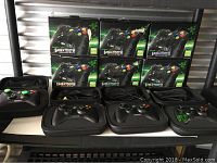 Image showing six Razer Sabertooth Xbox 360 controller boxes stacked alongside five controllers in their hard cases on a shelf.