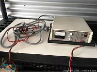 Full frontal view of the Fischer Galvanic Unit Model MD-1a showing the device on a black shelf with attached red and black wires.